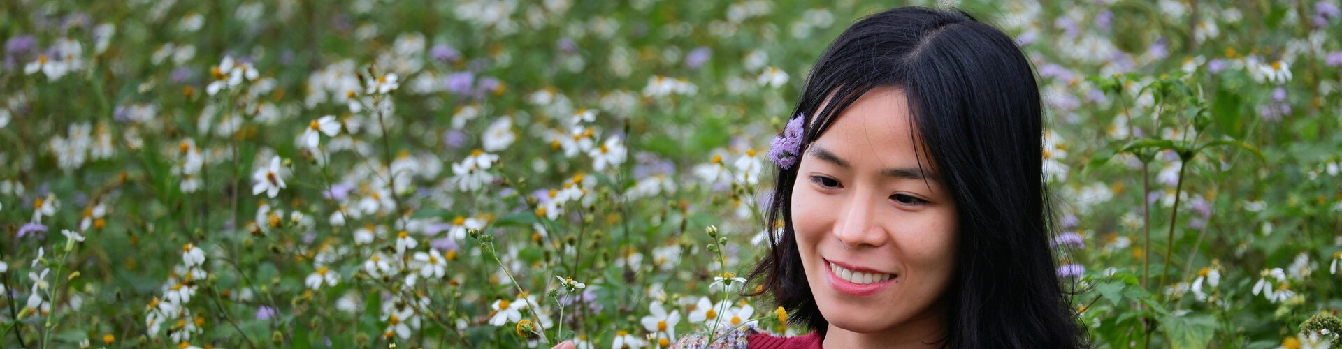 Mujer en un campo de flores, muy contenta y disfrutando de la naturaleza. Uno de los elementos más importantes para el disfrute de esta chica es el olor fresco y natural que le traen las flores. Uno de los beneficios del marketing olfativo es generar sensaciones similares en los clientes de un negocio.